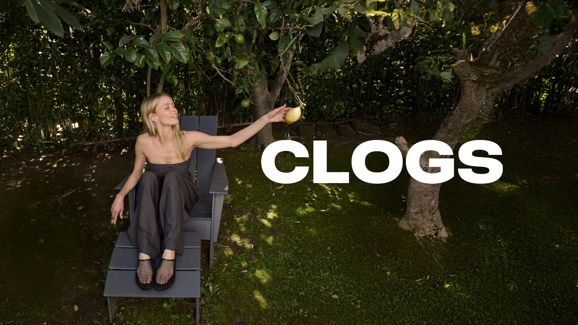 girl standing on the beach and squatting wearing bone colored fuzzy clogs. The word 'Clogs' is displayed in large text across the image.