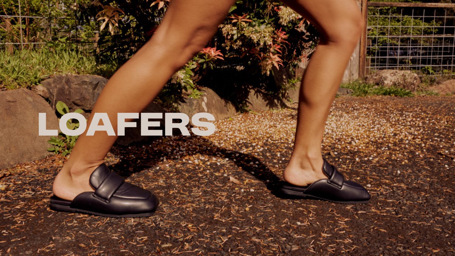 Close-up of black loafers walking on ground, with green plants in the background. The word 'Loafers' is displayed in large text across the image.
